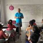 Volunteer pictured in front of the classroom and talking to the children.