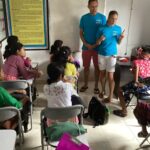 Two volunteers at the front of the classroom talking to the local children.