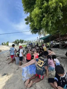 Volunteers and local children sitting by the beach together.